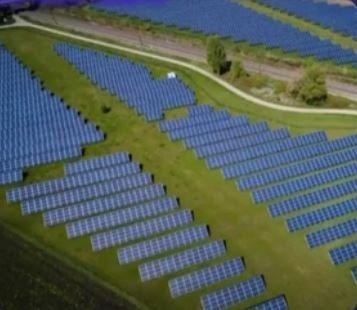 Aerial view of a solar farm with rows of solar panels on green fields.