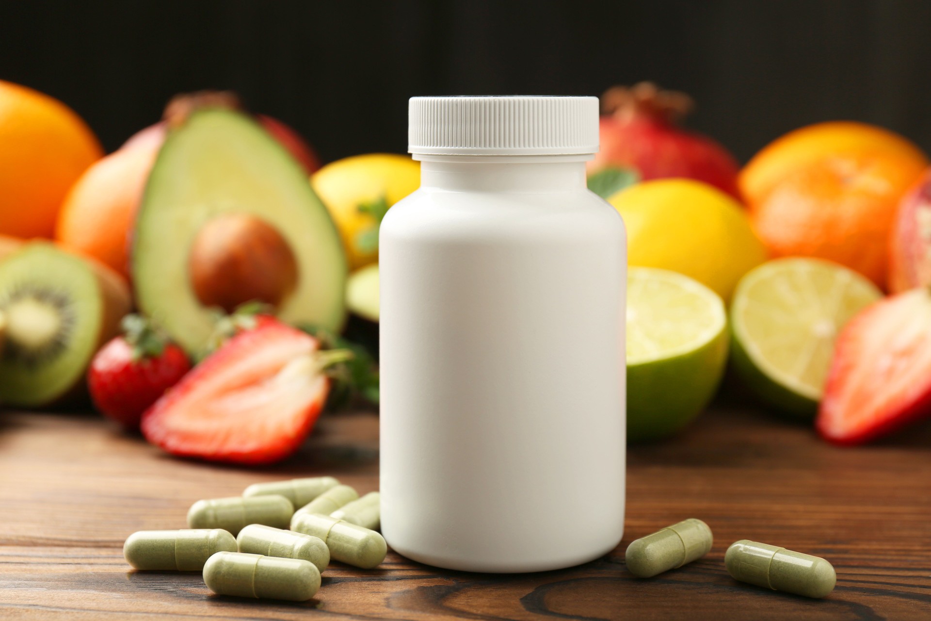 Vitamin pills, bottle and fresh fruits on wooden table, closeup